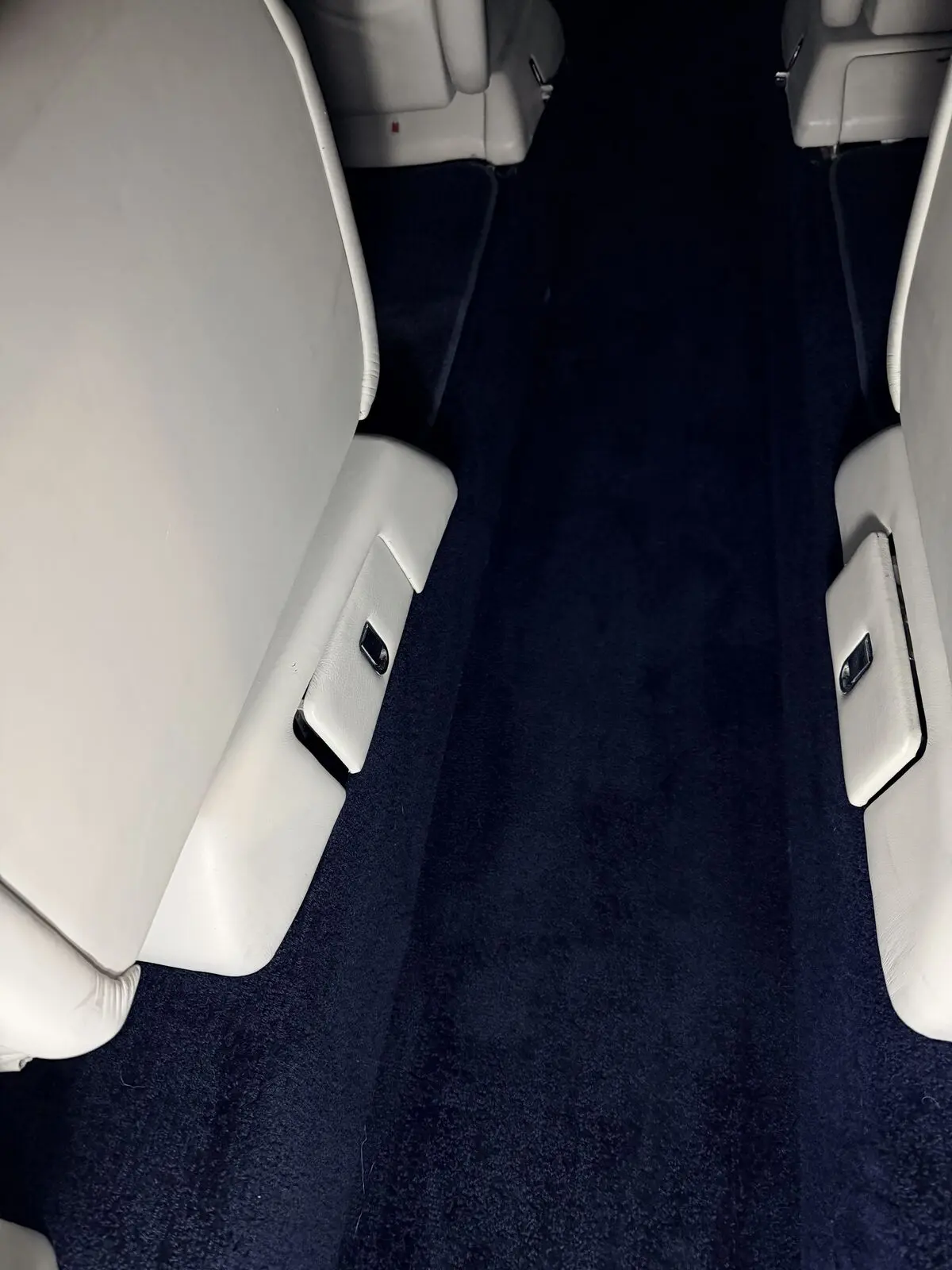 Private jet white leather seat with navy blue sidewall carpet and armrest detail after interior detailing